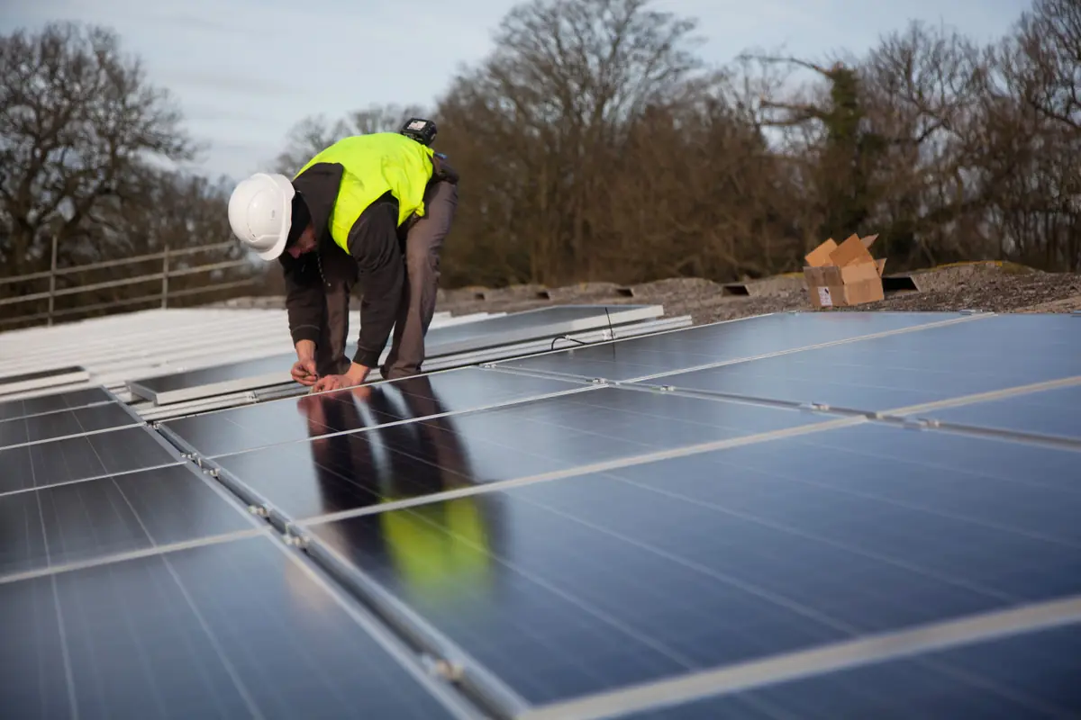 Installer in a hard hat and hi-vis vest securing a row of solar panels
