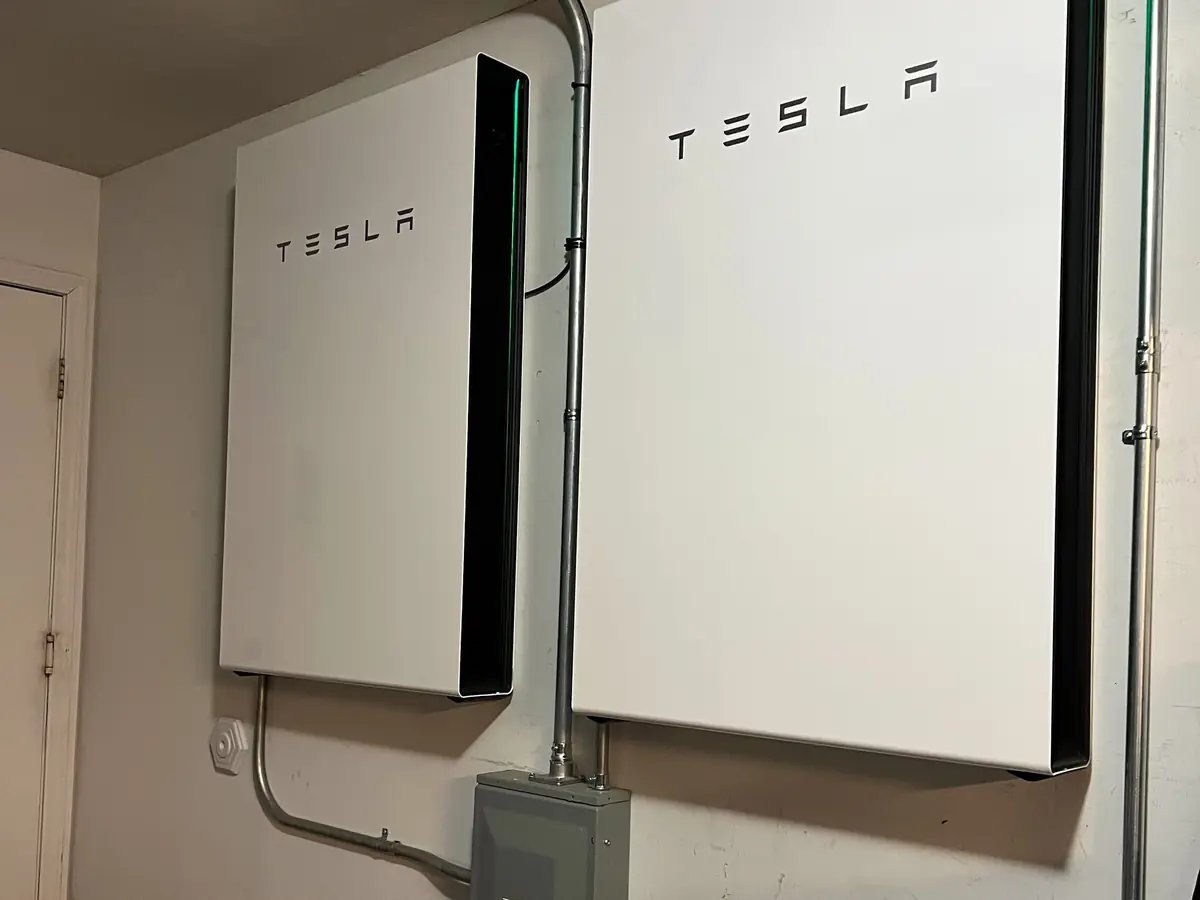 Two wall-mounted home battery units with a switch box in a garage